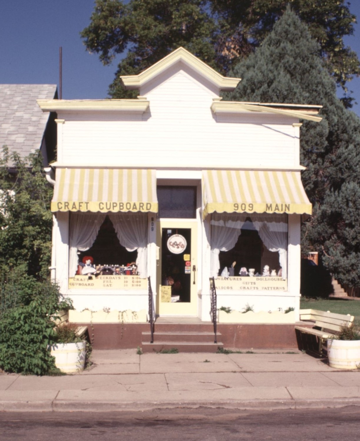 Shop front of the "Craft Cupboard" at 909 Main. A white building with yellow awnings.