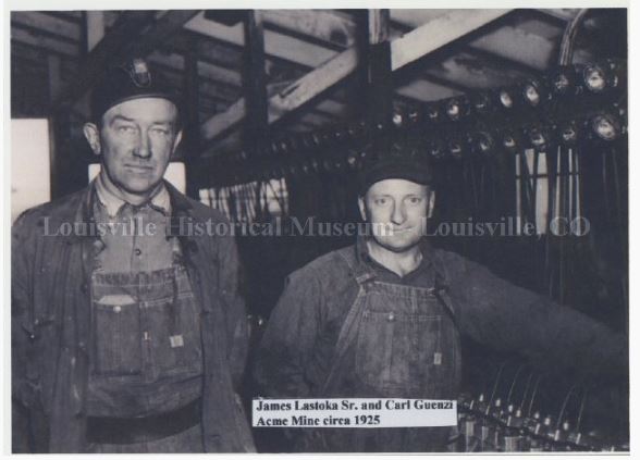 Two men in overalls standing in front of equipment from the Acme Mine