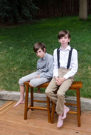 Two boys, one wearing suspenders, posing on wooden stools