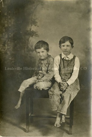 Old photo of two boys in overalls sitting on a wooden bench.