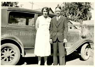 Old photo of man and woman standing in front of an automobile.