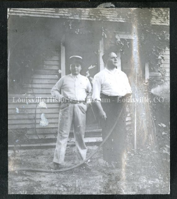 Eliseo Jacoe watering the lawn with son standing with hands on hips.