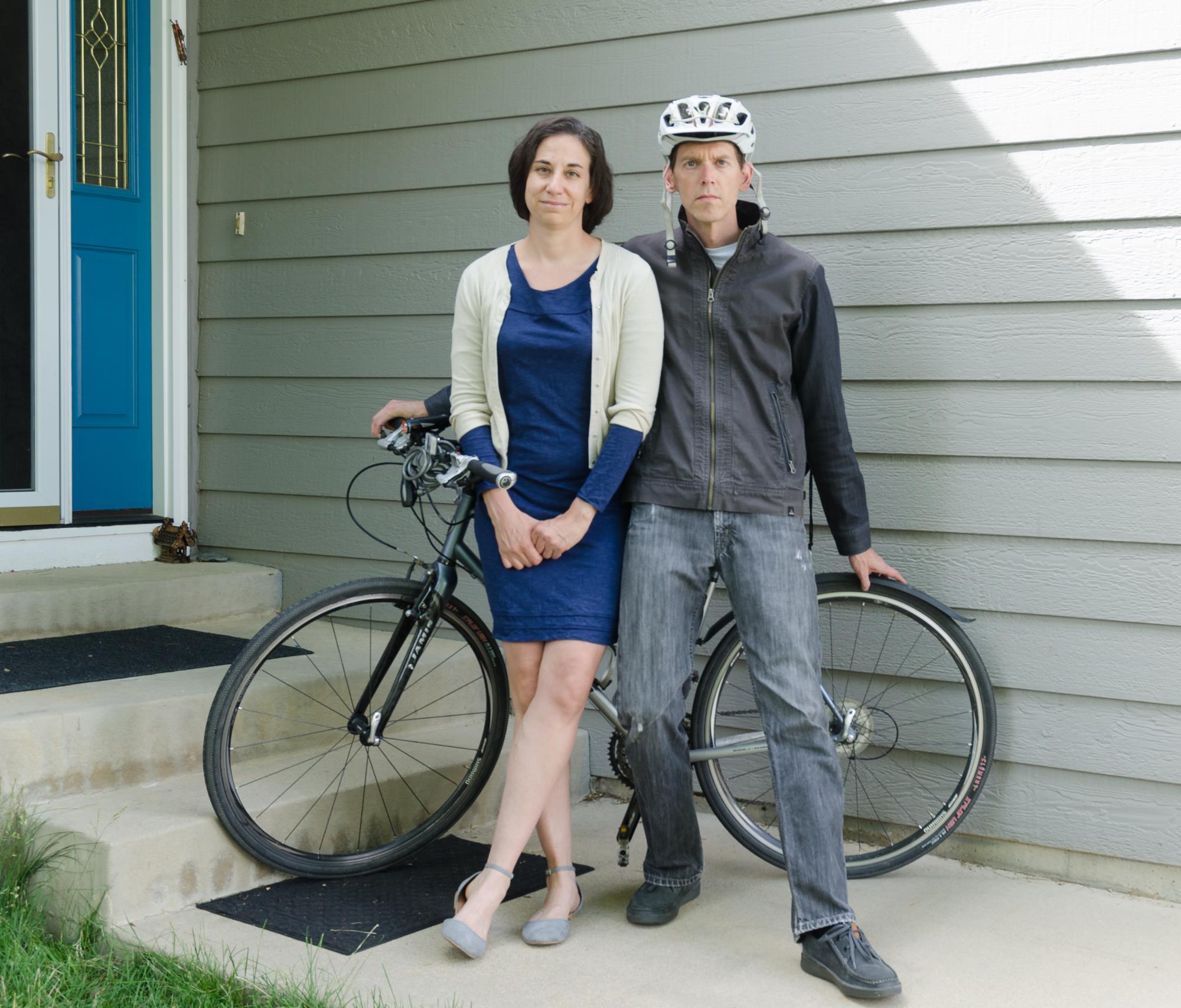 Man wearing windbreaker and bike helmet and woman leaning against a bicycle.