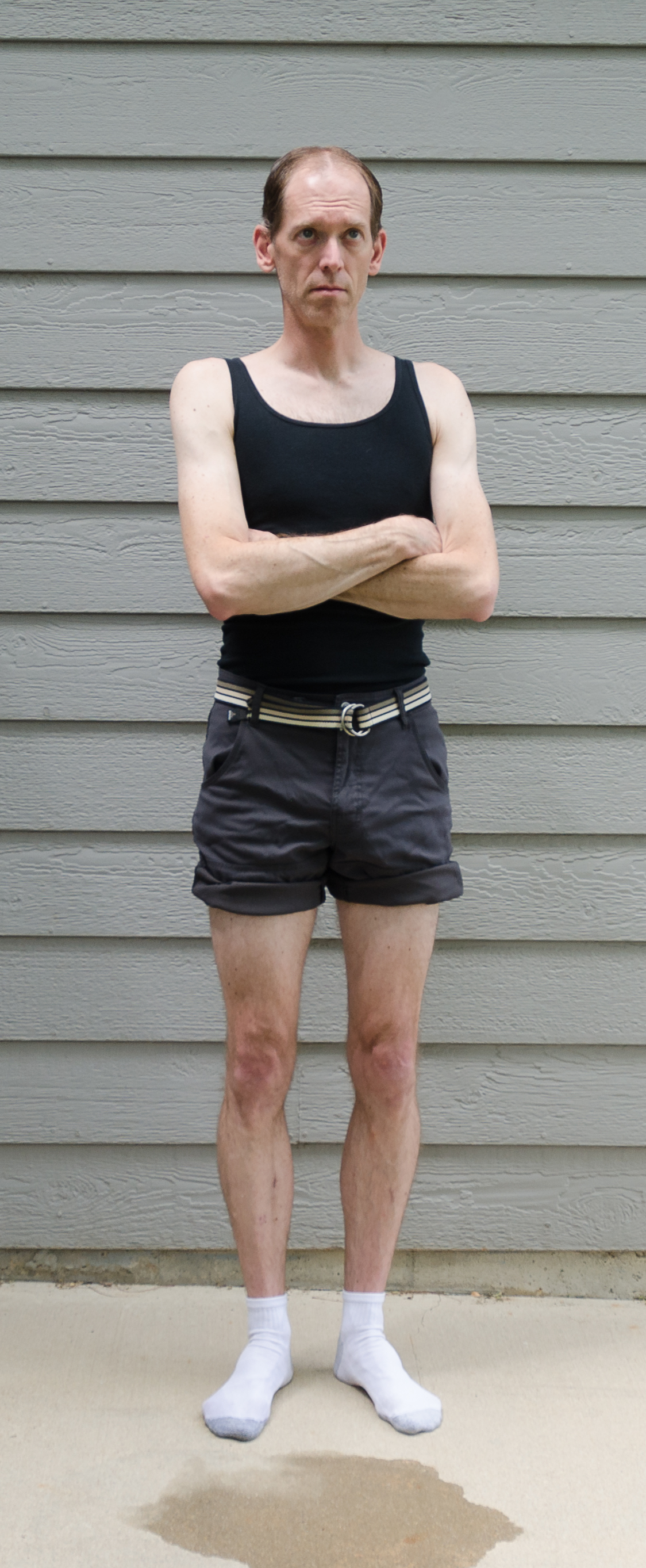 Man in tank top and shorts standing with arms crossed.