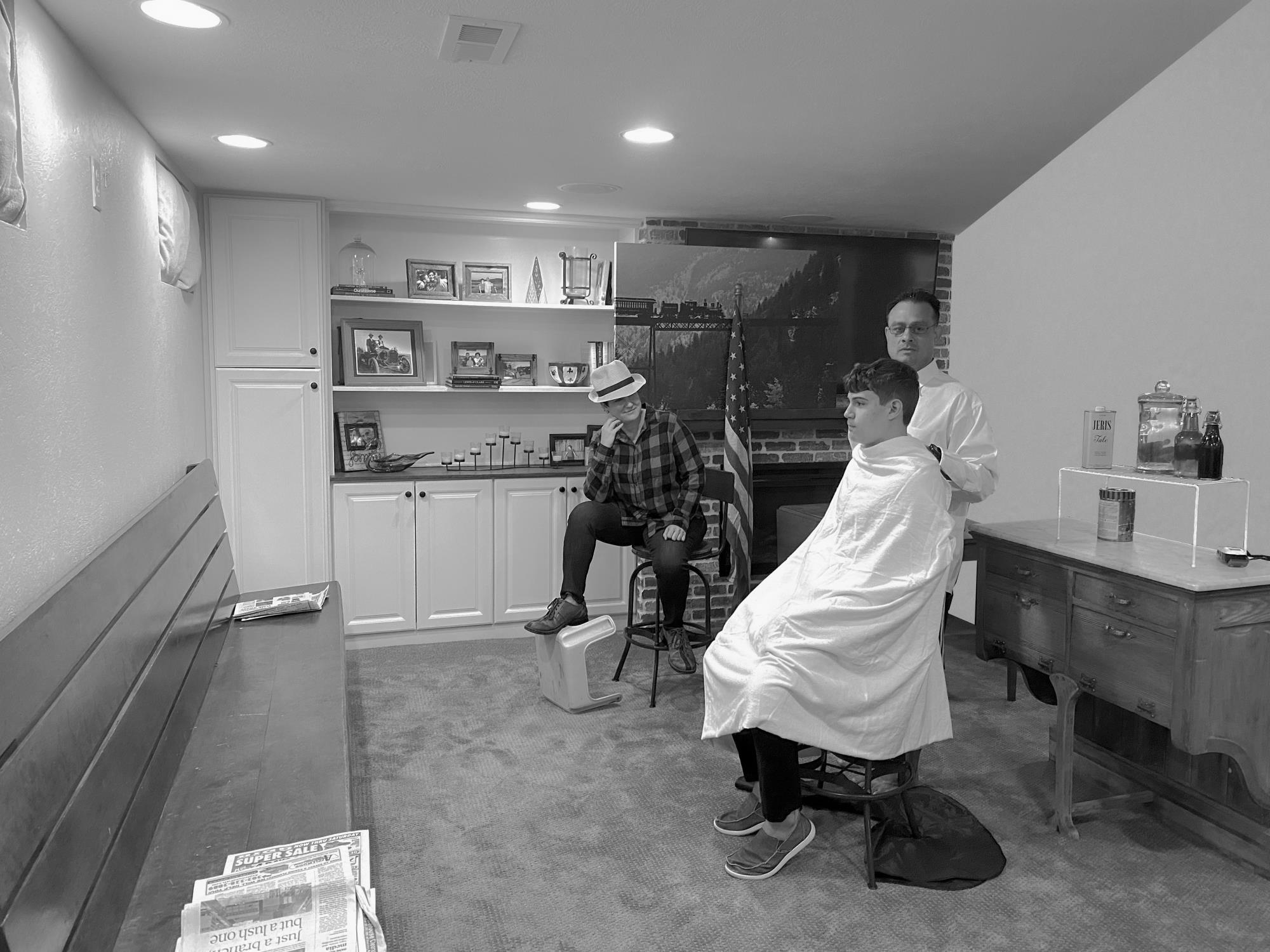 Interior of room with man posing as a barber and two teens sitting on stools.