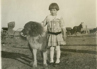 Small girls standing next to large fluffy dog.