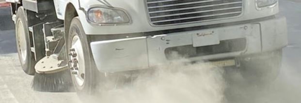 close up of street sweeper on road with dust