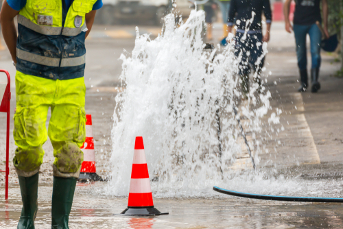 water coming up from street with hazard cones and city worker