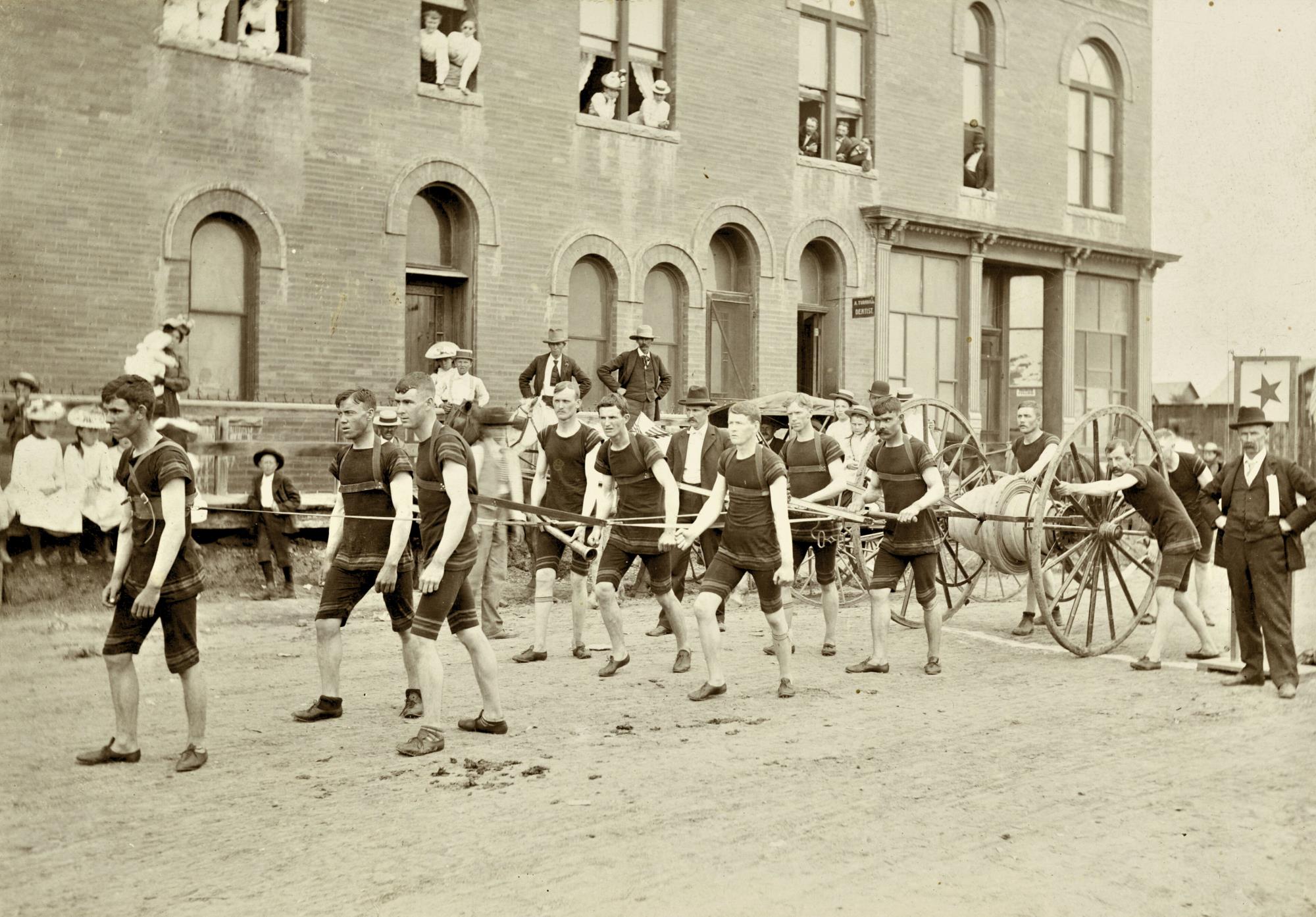 Men in harness pulling a hose cart for a volunteer firemen hose team