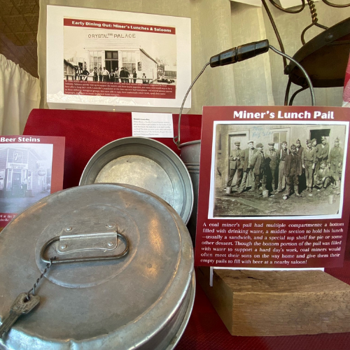 a metal lunch pail in an exhibit with a panel labeled "Miners lunch pail"