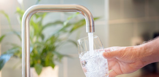 Photo of a hand holding glass under water flowing from faucet