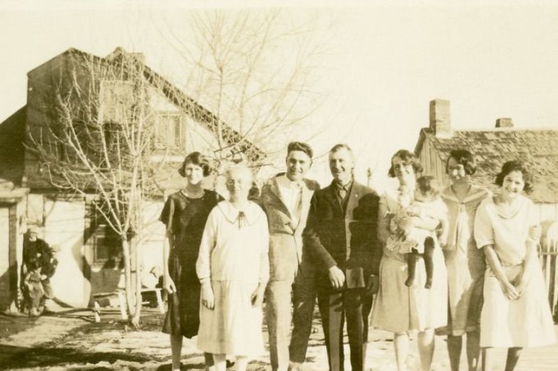 black and white photo of large family. Two houses shown in background.