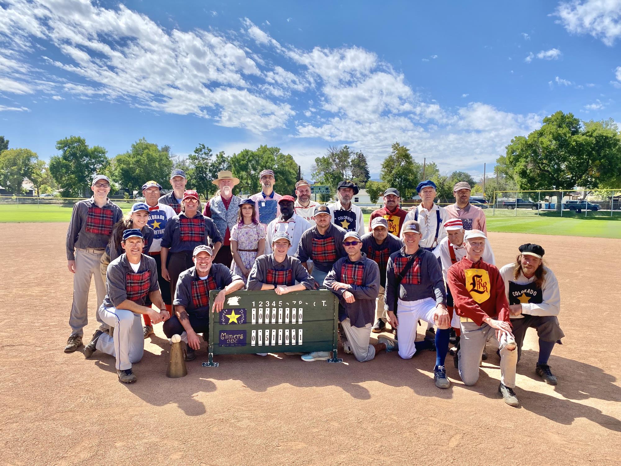 Photo of many baseball players in vintage uniforms around a scoreboard