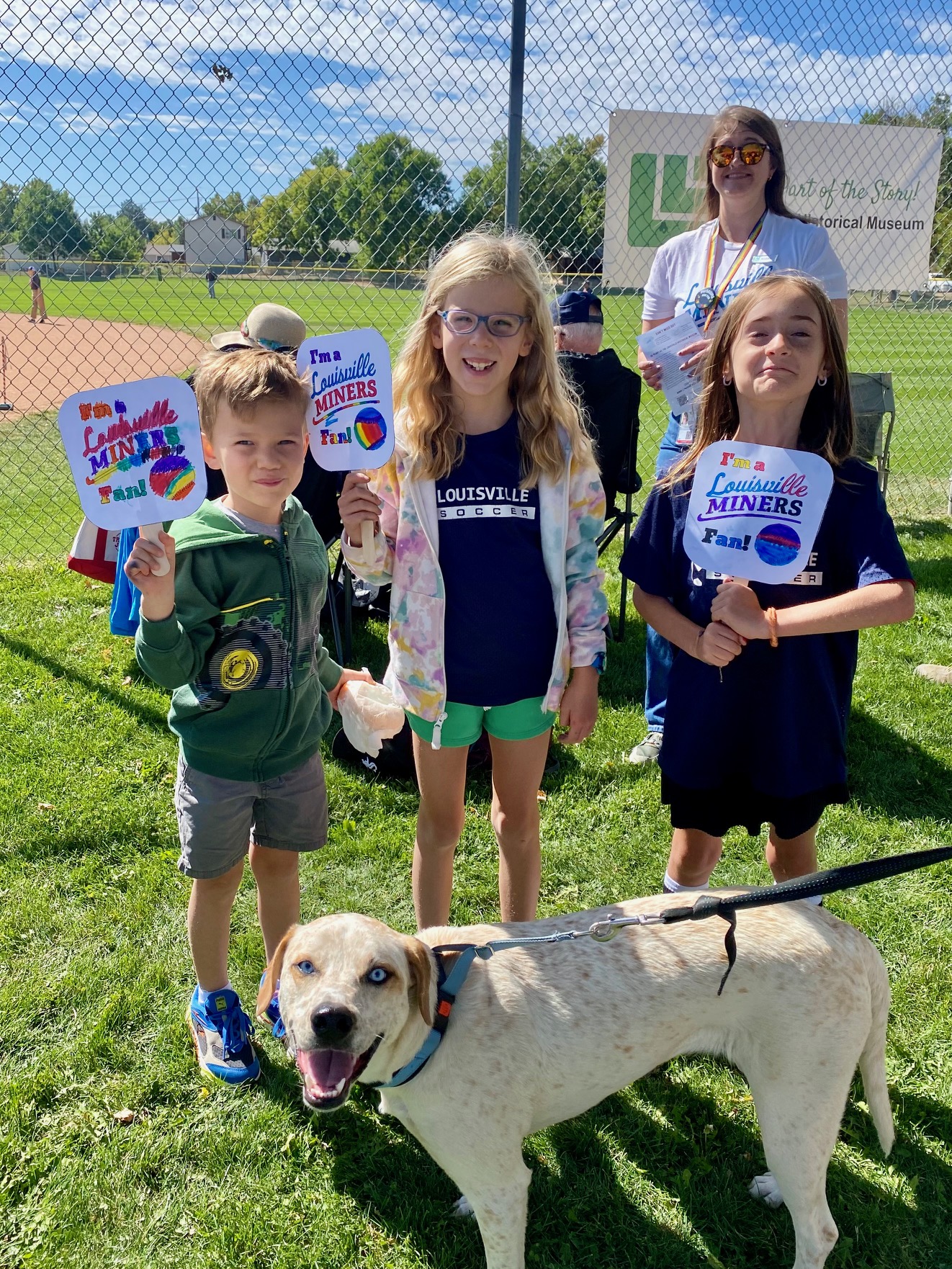 Three children hold signs reading "Louisville Miners" with a dog